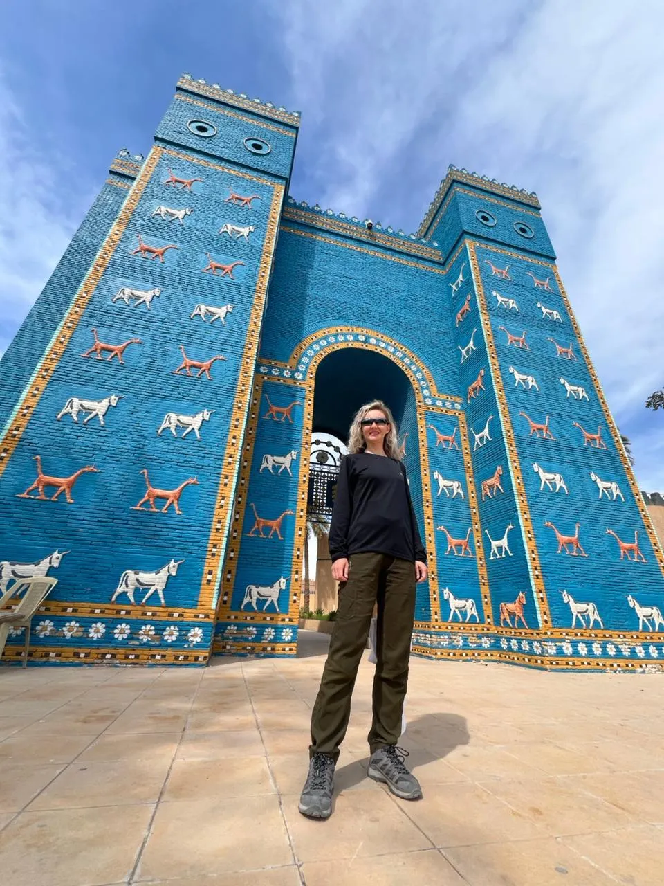 A visitor standing in the arch of the reconstructed Ishtar Gate at Babylon, rows of white bulls and sirrush dragons ranked across the blue-glazed brick.