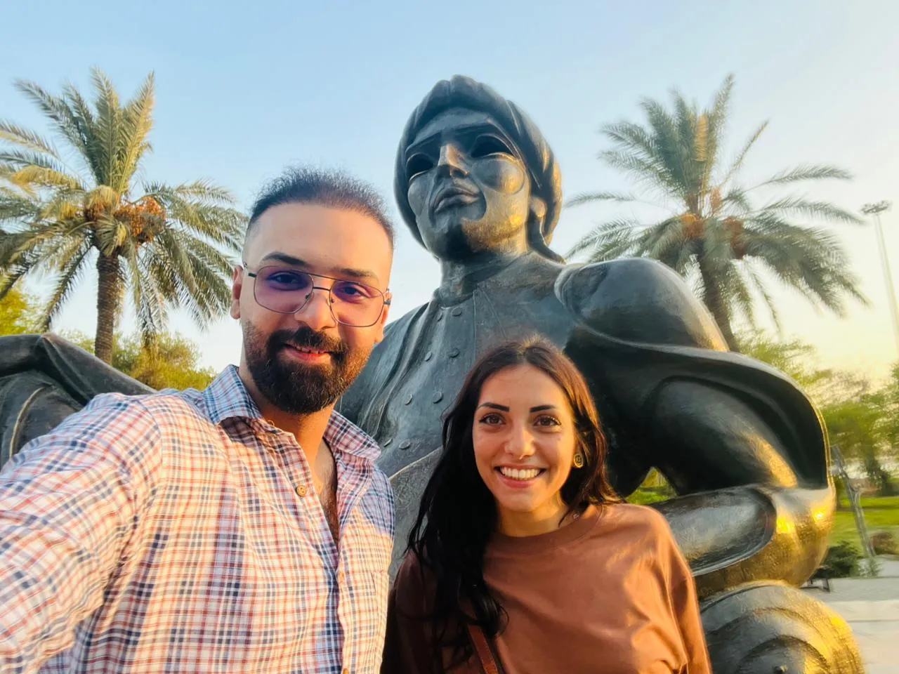 Two travellers beside a bronze figure set among date palms in a Baghdad park.