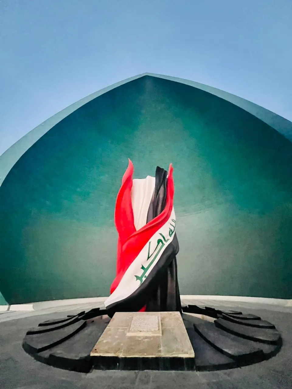 The Al-Shaheed Martyr's Monument in Baghdad, the Iraqi flag furled at the centre of its split turquoise dome.