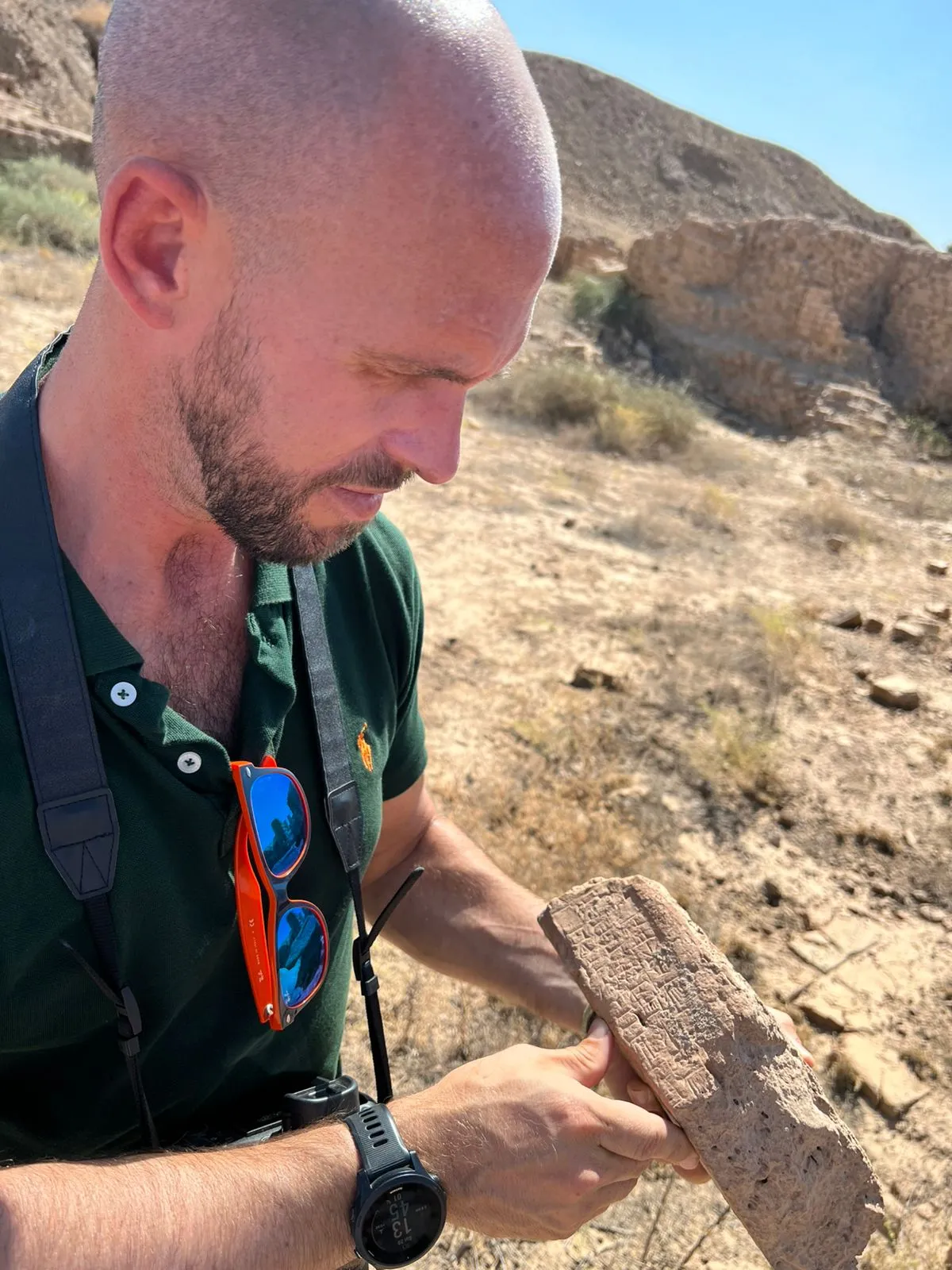 An archaeologist at an excavation site holding an inscribed clay tablet in both hands, its cuneiform wedges still sharp in the dried clay.