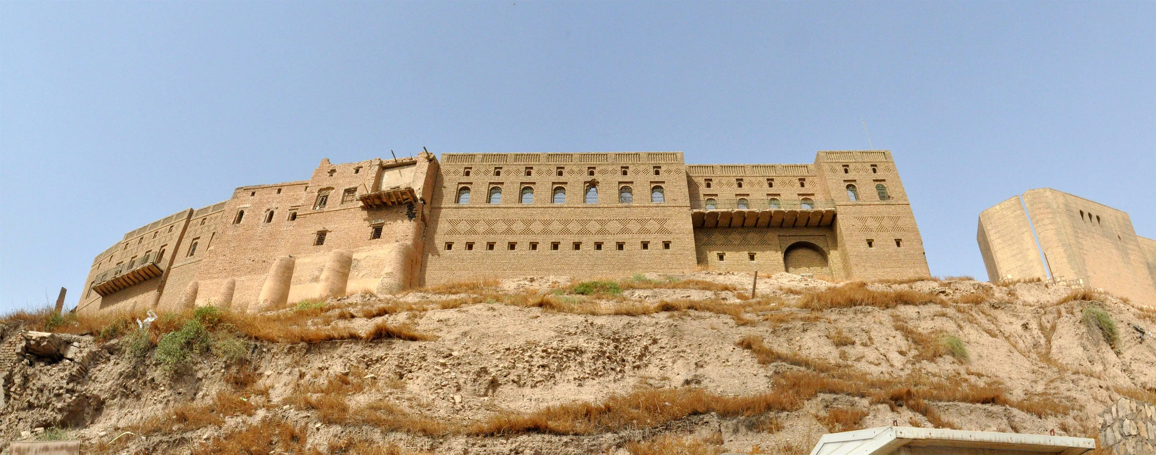 The Citadel of Erbil rising on its tell above the modern city, golden brickwork lit by low sun under a clear Kurdistan sky.