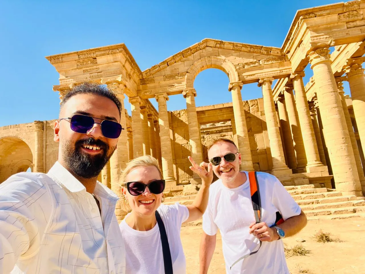 Travellers in front of the columned temple facade at Hatra, sunlit limestone against an open desert sky.