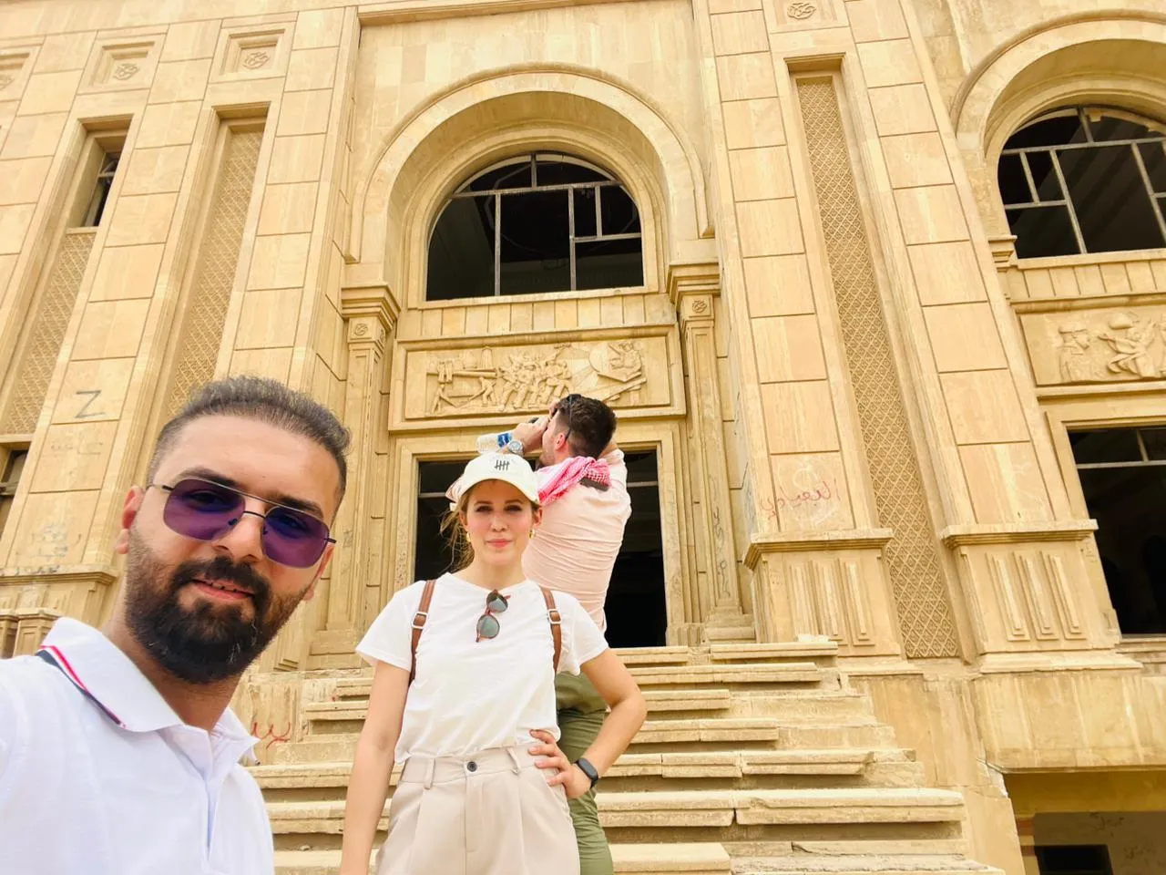 A family on the steps of a grand stone building, a carved relief set above its doorway.