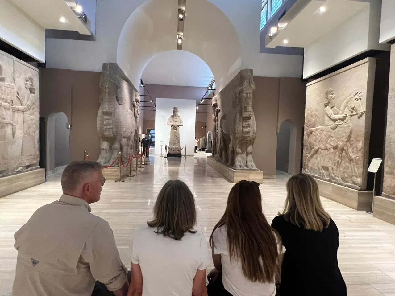 The Assyrian gallery of the Iraq Museum in Baghdad, winged lamassu bulls and carved stone reliefs flanking the hall as visitors look down it.
