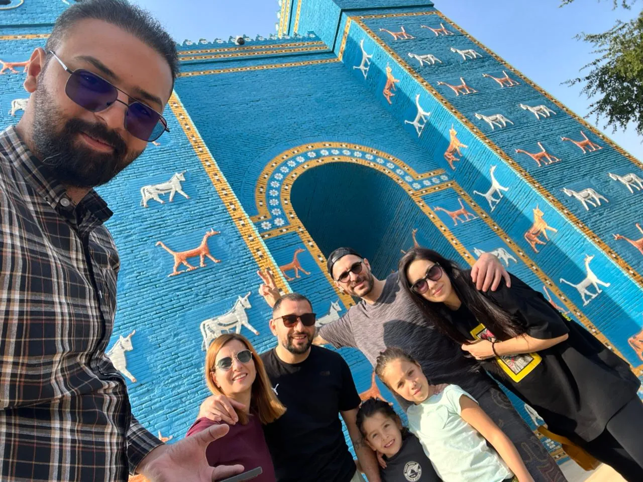 A guide and a family of travellers in front of the reconstructed Ishtar Gate at Babylon, its cobalt-blue brick ranked with bulls and dragons.