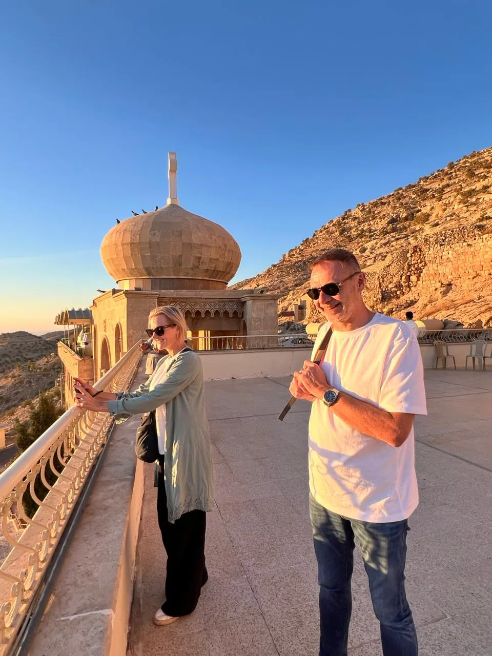 A domed hilltop shrine in northern Iraq at golden hour, bare mountain ridges rising behind its stone balustrade.