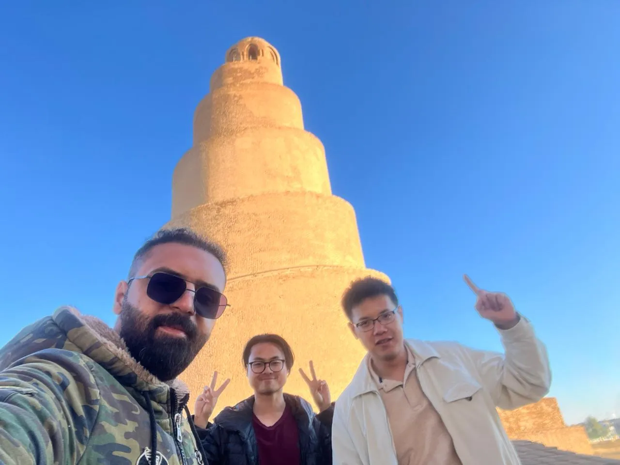 Three travellers at the foot of the Malwiya in Samarra, its spiral ramp winding up into a clear sky.