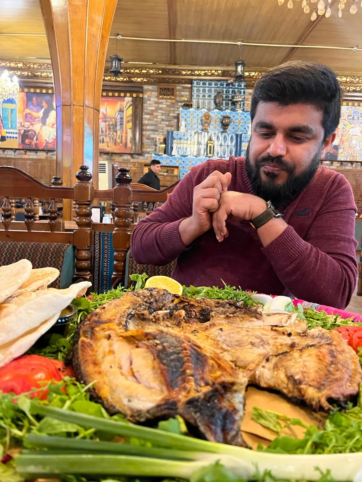 A whole masgouf fish split and grilled over wood, served on a bed of fresh herbs with flatbread and lemon.