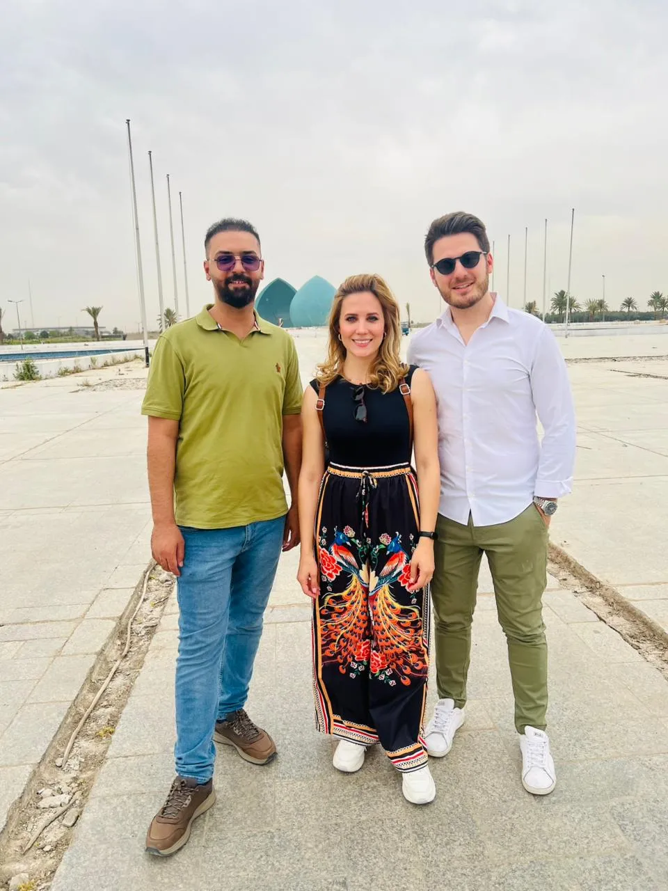 Three travellers on an esplanade with a turquoise dome standing across the water behind them.