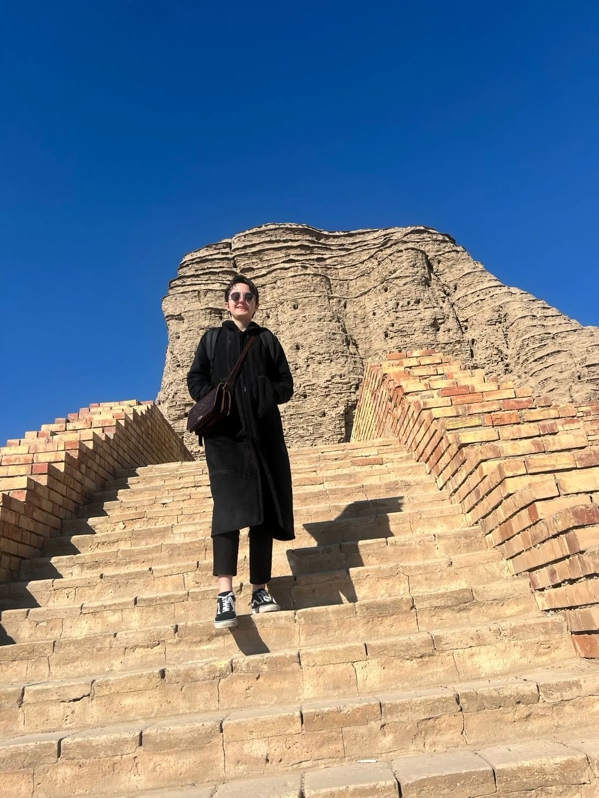 A visitor climbing the great central staircase of the Ziggurat of Ur, buttressed brick terraces rising on either side.